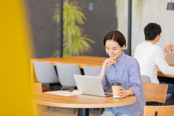 カフェ型のワークスペースでコーヒーを飲みながら仕事をしている女性